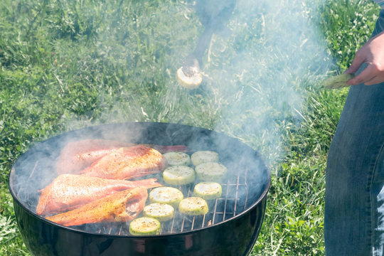 Picnic outdoors in the summer. Cooking on a round grill fish sea bass and zucchini slices