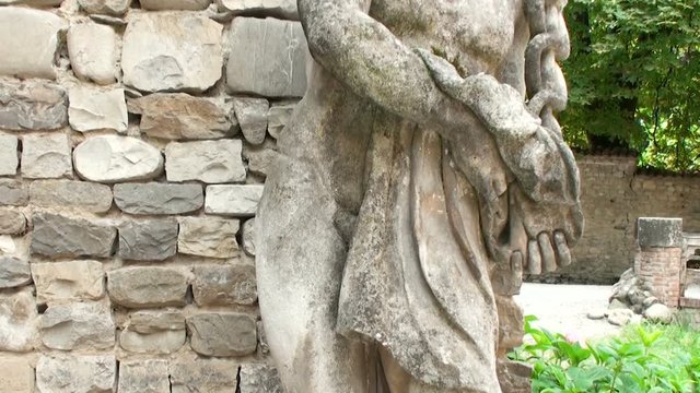 Ancient statue of gothic naked muscular warrior man with a hat with wings, in one medieval village in Italy