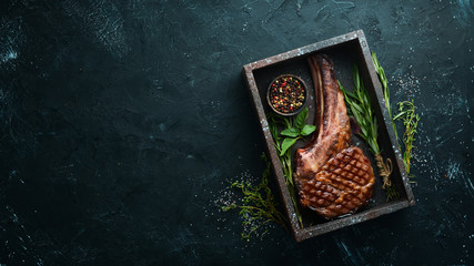 Grilled cowboy beef steak, herbs and spices on a black stone background. Barbecue. Top view. Free...