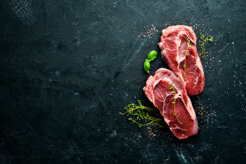 Raw Steak Ribeye. On a black stone table. Top view. Free space for your text.