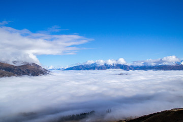 Fototapeta na wymiar Low clouds or fog (inversion) above lake Wakatipu and Queenstown valley. View of the scenic road and snow covered peaks of Single cone, Cecil Peak and Mount Nicholas. Panoramic landscape. New Zealand.