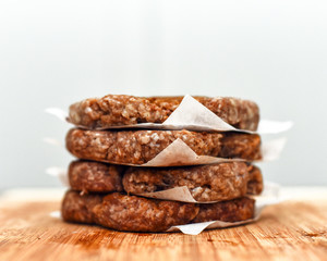 Raw hamburger patties stacked on wooden cutting board