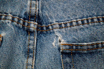 Top view of worn out double sewn seams and frayed hole on pocket of old blue jeans.