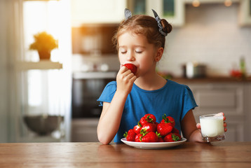 happy child girl eating strawberries with milk