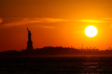 statue of liberty at sunset with silhouette and sun and orange sky