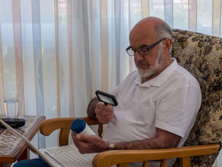  Old man  with magnifying glass reading on the jar with vitamines