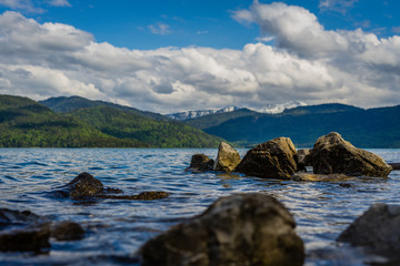 Fototapeta na wymiar low angle view over water with many rocks in the foreground and mountains in background