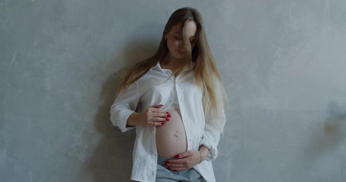 Happy caucasian pregnant women with big belly standing and rubbing her belly. 60 fps