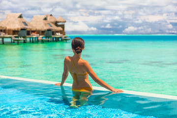 Luxury overwater bungalow hotel room with infinity swimming pool woman looking at blue ocean view....