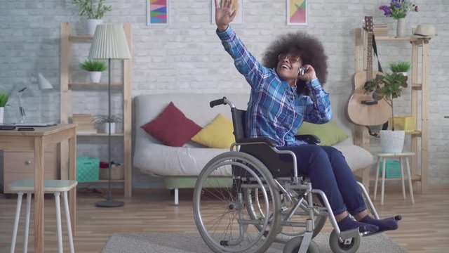 cheerful disabled african american woman with an afro hairstyle in a wheelchair in headphones listening to music