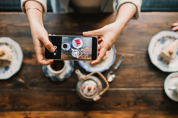Top view of woman taking a photo of cake and tea in coffee shop
