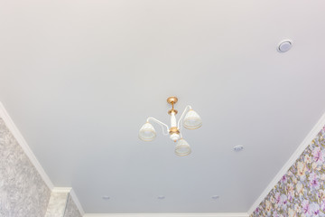 Stretch matte ceiling in the room with a chandelier and spotlights, with natural light