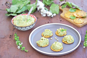 Snack, green pea spread with almonds and basil on unsweetened crackers on a brown clay plate. Healthy snacks.