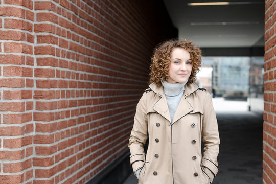 Portrait of smiling woman with curly hair wearing beige trench coat and turtleneck pullover