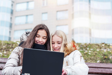 two young beautiful students studying by laptop on the street in the park