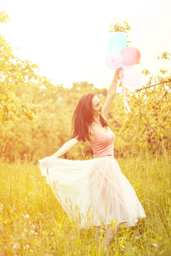  girl running and jumping on summer field with colorful air balloons over sunset . girl running and jumping on summer field with colorful air balloons over Sunset 