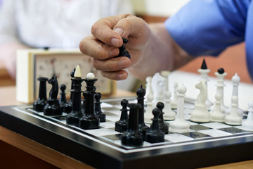 An elderly man plays chess and takes the figure of the enemy