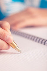 Teen writes black yellow pen in a checkered notebook