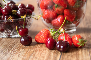 Fresh organic sweet cherries and strawberries in a glass bowls on wooden table