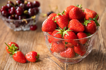 Fresh organic sweet cherries and strawberries in a glass bowls on wooden table