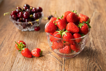 Fresh organic sweet cherries and strawberries in a glass bowls on wooden table