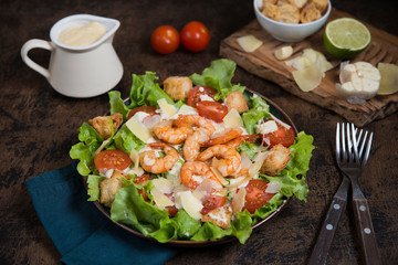 Caesar salad with shrimp on a dark wooden background.