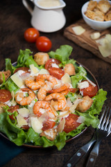 Caesar salad with shrimp on a dark wooden background.