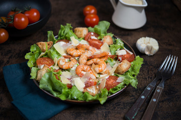 Caesar salad with shrimp on a dark wooden background.