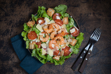 Caesar salad with shrimp on a dark wooden background.