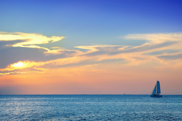 Colorful seascape image with shiny sea and sailboat over cloudy sky and sun during sunset in Cozumel, Mexico