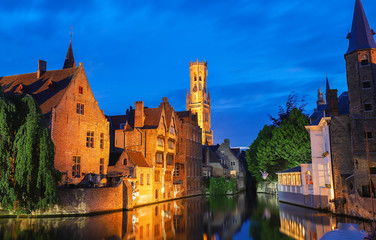 Fototapeta premium Famous view of Bruges tourist landmark attraction - Rozenhoedkaai canal with Belfry and old houses along canal with tree in the night. Belgium