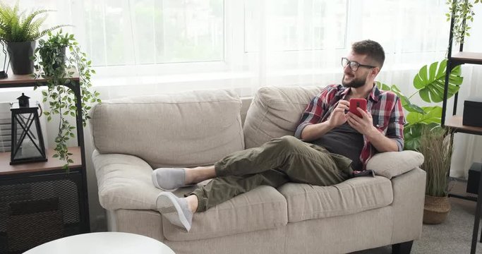 Smiling young man using mobile phone on sofa at home