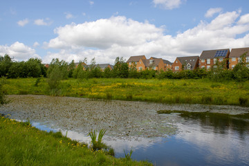 Fototapeta na wymiar Small lake over looking a suburban housing estate in the UK, taken on a part cloudy sunny day 