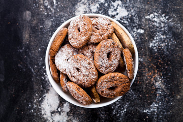 Fresh baked chocolate chip and oat fresh cookies with sugar powder heap in white bowl on black background.