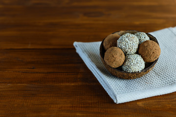 Energy balls of dates, nuts, cocoa and sesame on a wooden table. Raw dessert in a coconut shell, with a copy space