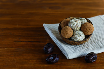 Energy balls of dates, nuts, cocoa and sesame on a wooden table. Raw dessert in a coconut shell, with a copy space