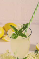 Elder lemonade - healthy and refreshing summer drink. Close up of homemade elderflower syrup in a bottle with elderflowers. Summer drink Hugo Champagne drink with elderflower syrup, mint and lime.