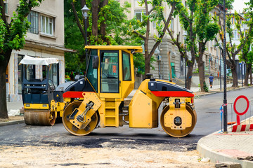 Yellow roller for tamping asphalt at the site of road construction works on a city street on a summer day. Road-building machinery.