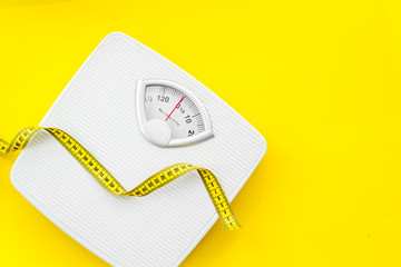 Diet concept with scale and measuring tape for weight loss on yellow background top view