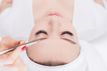Beautiful young girl with long eyelashes tweezing her eyebrows in a beauty salon. Woman doing...