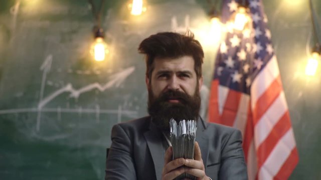 Man in a suit beats wad of money from which flies dust. Dirty money. Background of the American flag and a chart drawn by chalk on a board. Background. Bribery, corruption and venality concepts.