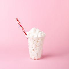 Plastic shake glass with straw full of sugar cubes on pastel pink background. Unhealthy drink concept. Minimal, vertical, side view.