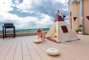 happy young boy, kid playing near the textile wigwam tent on the summer patio © Olesia Bilkei
