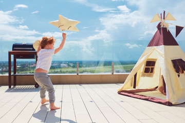 happy young boy, kid playing near the textile wigwam tent on the summer patio © Olesia Bilkei