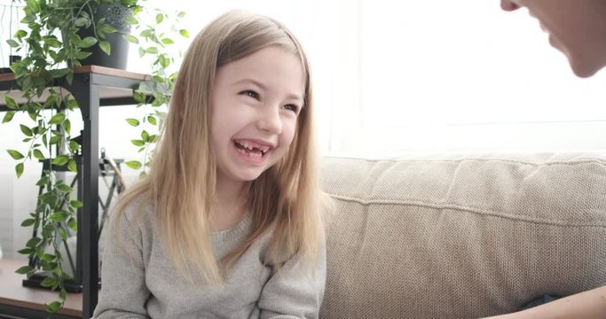 Cheerful little girl tickled by her mother in the living room