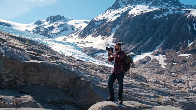 Bearded traveler with a backpack takes pictures of the glacier in Norway