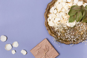 Dry petals of white roses and gypsophila on a beautiful antique tray, a gift wrapped in craft paper on a blue background. Place for text.