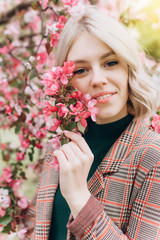 Close up portrait of young pretty caucasian curly blondie model posing outdoors in pink blossom garden. Beauty, nature concept