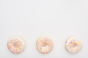 top view of sweet whole doughnuts with sprinkles near bitten one on white background