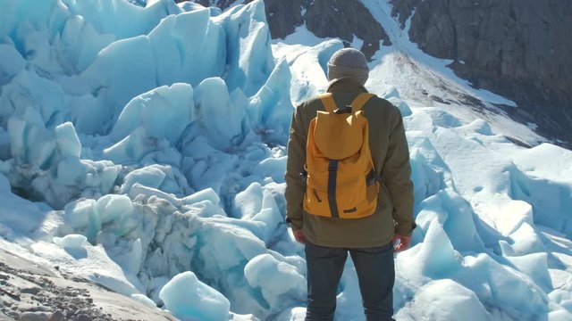 A tourist with a yellow backpack looks at the Svartisen glacier in Norway.